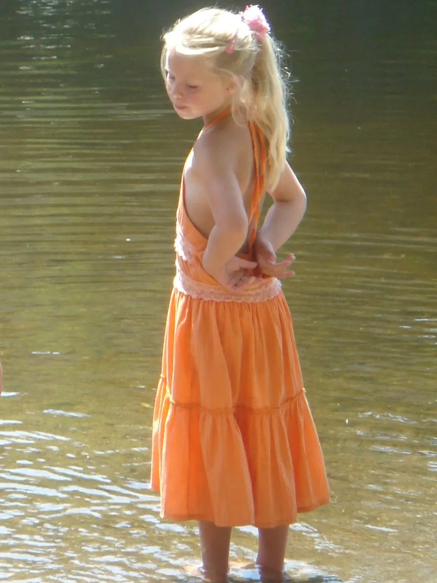 Eva als jong meisje in een oranje jurk, tot haar enkels in het water