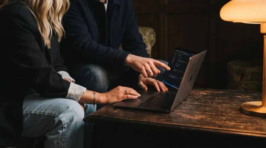 Twee mensen samen achter een laptop aan een houten tafel